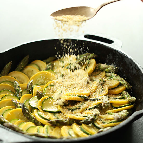 Sprinkling vegan parmesan cheese onto a skillet of Zucchini Gratin