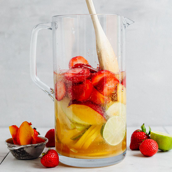 Using a wooden spoon to stir fresh fruit for making White Sangria